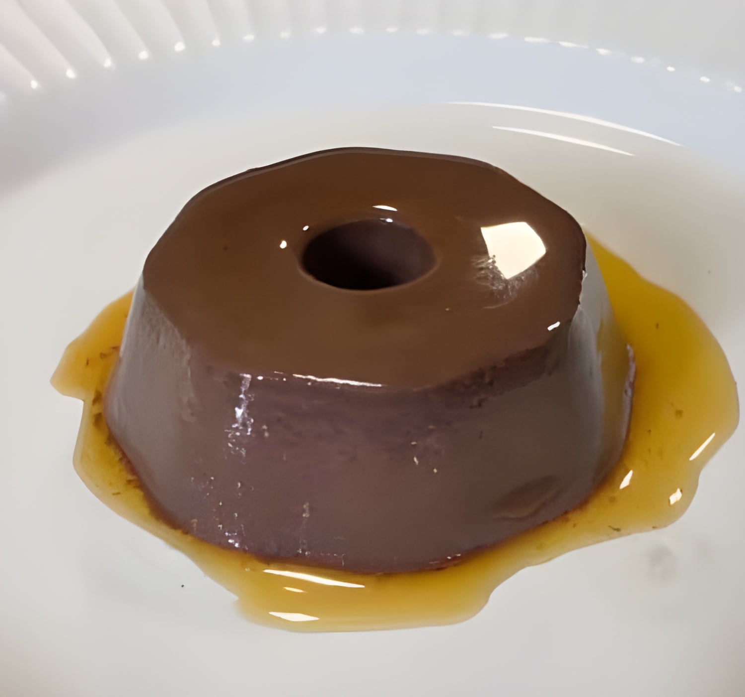Pudim belga preto com calda dourada sobre prato branco